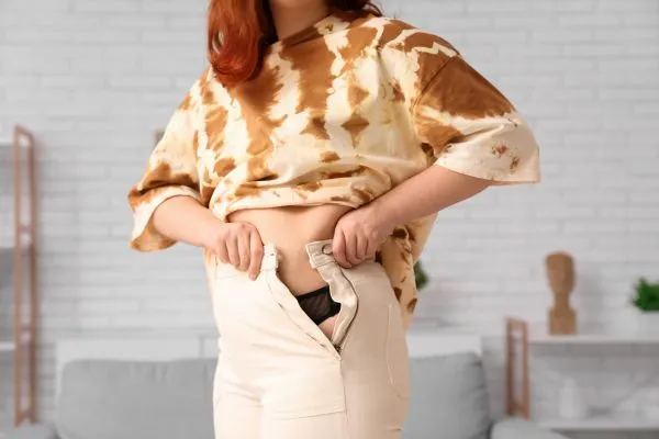Image of woman trying to do her trousers up after pregnancy weight gain Fairfield